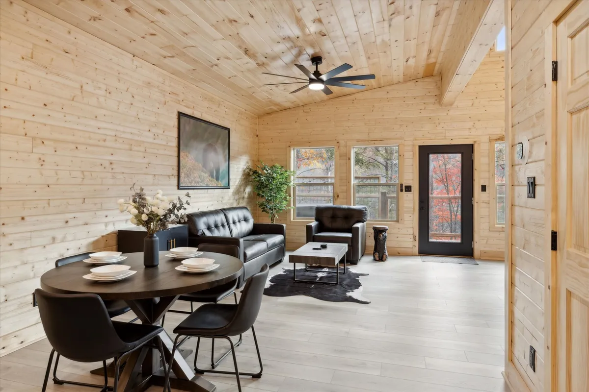 A comfortable interior scene featuring a dining table set for a meal, plush leather sofas arranged for conversation, and large windows letting in natural light. Decorative plants and artwork on the wall add a homely, inviting touch, creating a sense of togetherness.