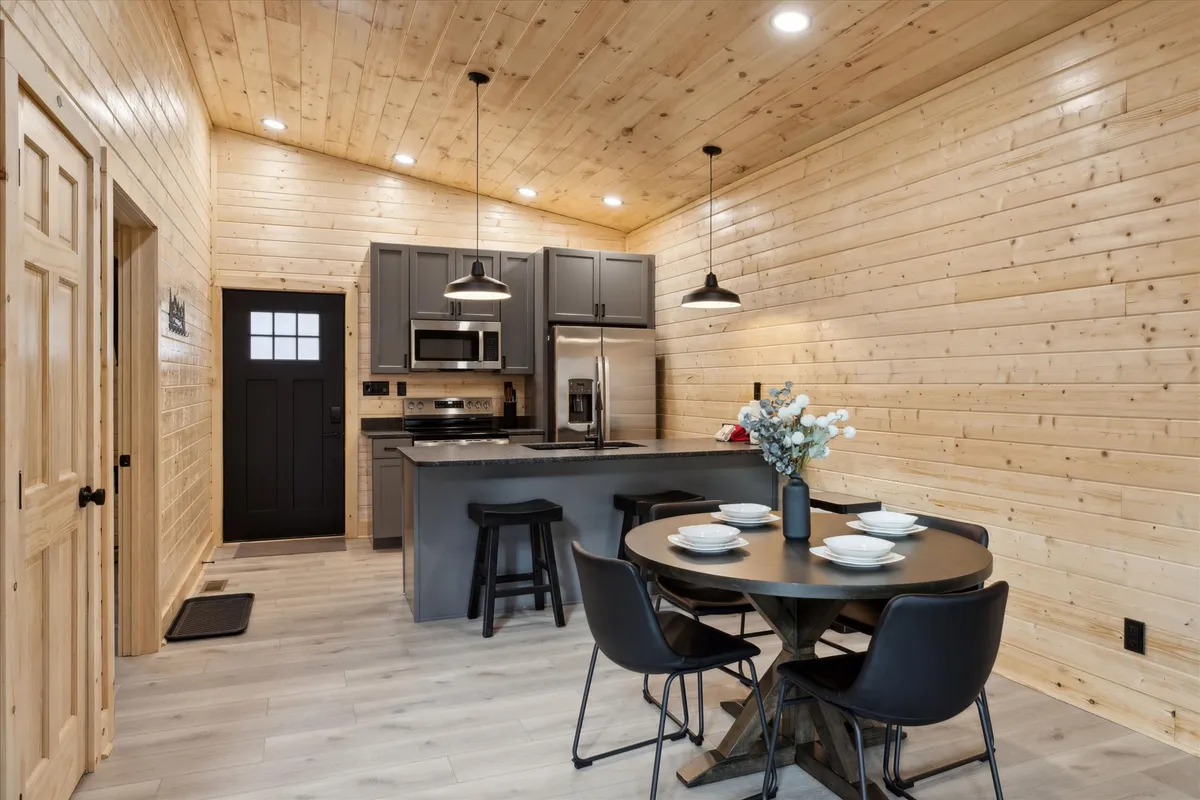 A well-designed kitchen and dining area with a kitchen island, a spacious dining table, and wooden walls illuminated by pendant lights. The atmosphere is both stylish and functional, offering plenty of room for meal preparation, dining, and socializing.