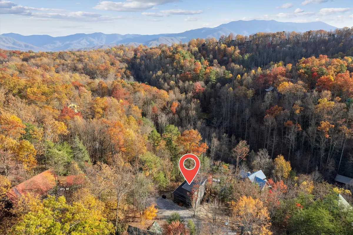 A wide view of a cozy cabin set against a breathtaking mountain range with vibrant autumn foliage. The cabin is positioned to showcase its easy access to nearby trails, and the overall mood is serene, hinting at outdoor exploration and relaxation after a day at local attractions.