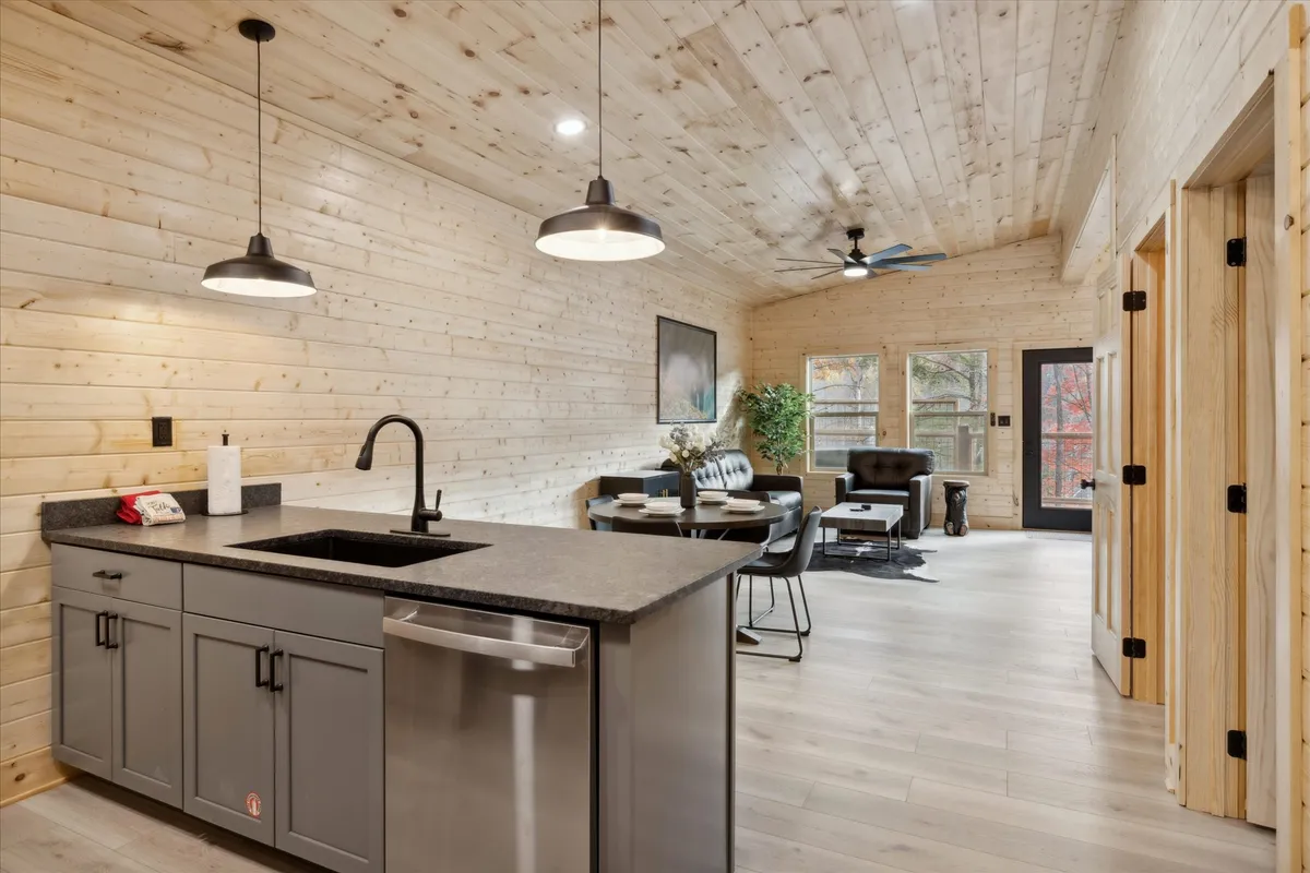 A spacious, open-concept living area that seamlessly connects the kitchen, dining area, and a cozy seating zone. The large windows flood the space with natural light, and the kitchen features a central island with sleek countertops. Multiple black chairs provide ample seating for gatherings, and the overall décor is warm and welcoming.