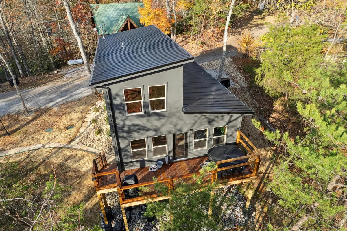A wide exterior view of the modern cabins with a spacious deck area surrounded by trees. The deck features a cozy fire pit area designed for group gatherings, with ample seating for guests to relax and socialize in the peaceful forest setting.