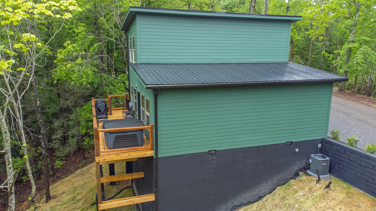 An inviting green cabin exterior with a wooden deck nestled among tall trees. The scene emphasizes the seamless transition from outdoor exploration to a cozy base camp, perfect for morning coffees or evening stargazing.